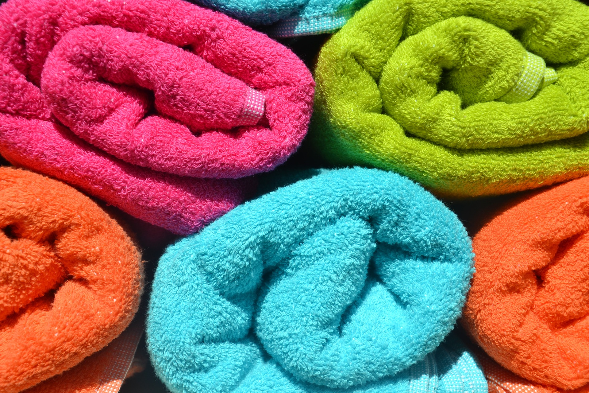 Bilden visar flera frottéhandukar i olika färger. En frottehandduk är praktisk både för badrummet och vid badstranden.